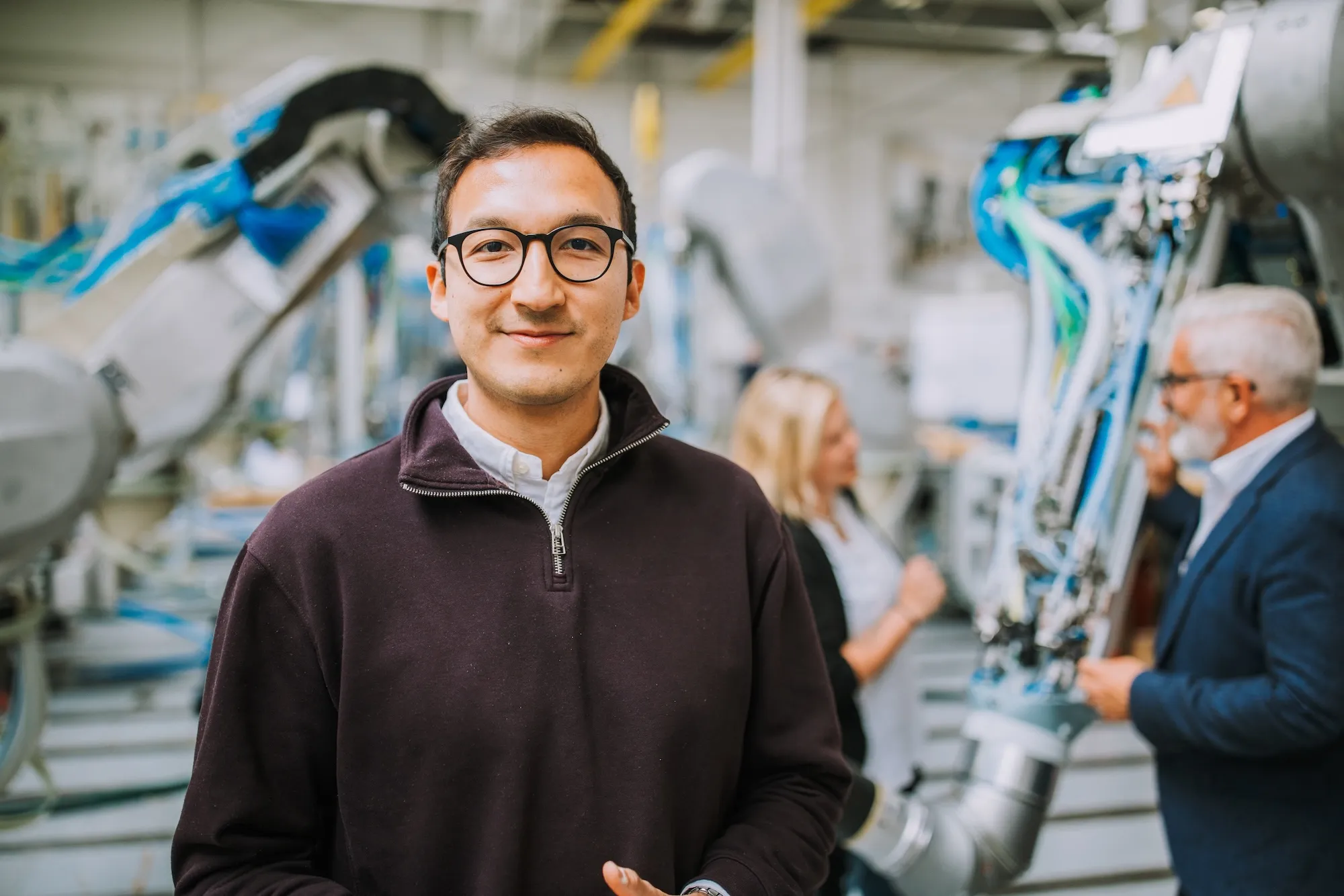 Engineer operating an industrial robot arm with a control device in a factory setting.